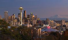 the seattle skyline is lit up at night with snow capped mountains in the back ground