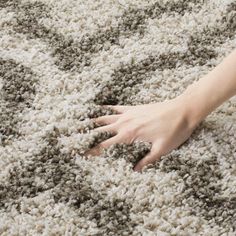 a woman's hand is on top of a shaggy rug with grey and white colors