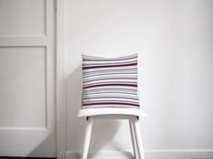 a white chair sitting in front of a door with a striped pillow on top of it