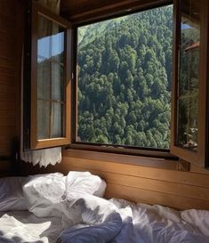 an unmade bed sitting in front of a window with mountains out the window behind it