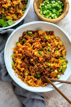 two bowls filled with noodles and vegetables next to chopsticks on a table top