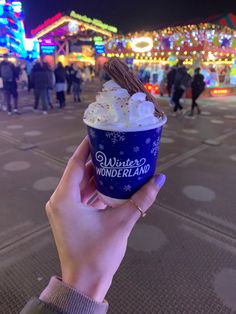 a person holding up a cup of ice cream in front of an amusement park at night