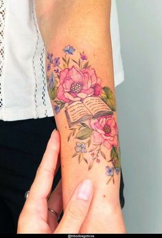 a woman with a book and flowers tattoo on her arm is holding an open book