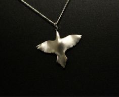 a silver bird necklace on a black surface