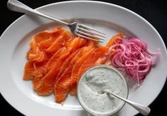 a white plate topped with salmon and onions next to a small bowl of ranch dressing