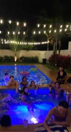 a group of people sitting around in a swimming pool at night with lights on the ceiling