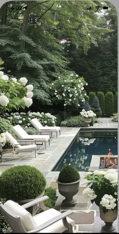 a pool surrounded by lots of white flowers and greenery next to some lawn chairs