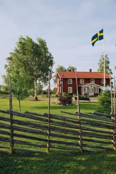 a wooden fence in front of a red house with a swedish flag on the top