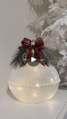 a white vase with a red bow and lights on it sitting on a table next to a christmas tree