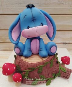 a blue and pink elephant figurine sitting on top of a tree stump next to mushrooms