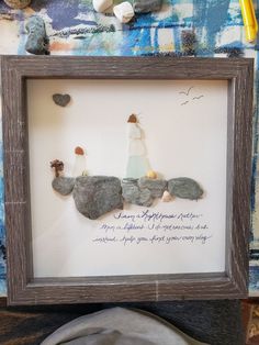 a person is holding up a framed artwork with rocks and writing on the paper in front of them