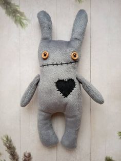 a gray stuffed animal with yellow eyes hanging on a white wooden wall next to pine branches