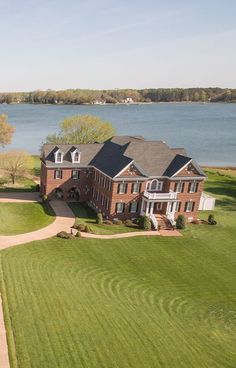 an aerial view of a large brick house in front of a body of water and trees