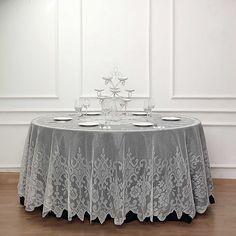 a round table with white lace on it in front of a wall and wooden floor