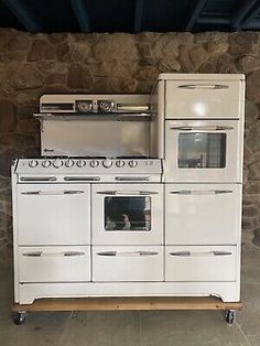 an old fashioned white stove and oven in a room with stone wall behind the stove