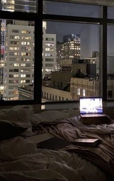 an open laptop computer sitting on top of a bed in front of a large window