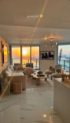 a living room filled with lots of furniture and large windows overlooking the ocean at sunset