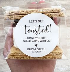 a hand holding a bag of cookies with the words, let's get toasted thank you for celebrating with us