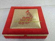 a red and gold box with a golden peacock on the lid sitting on a white surface