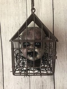 a creepy looking face in a cage hanging from a chain on a white wooden wall