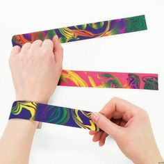 two hands are holding colorful wristbands with designs on them and one hand is pointing at the other