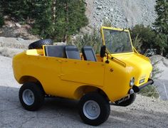 a small yellow vehicle parked on the side of a road next to some rocks and trees