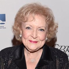 an older woman with blonde hair wearing a black jacket and diamond earrings smiles at the camera