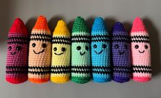 four crocheted crayons are lined up in a row with faces drawn on them