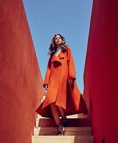 a woman in an orange coat is walking down some stairs with her hands on her hips