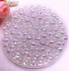 small round beads are in a plastic container next to flowers and pearls on a white surface