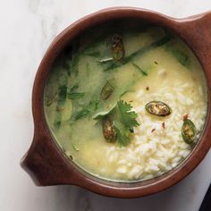 a wooden bowl filled with white rice and green vegetables on top of a marble counter