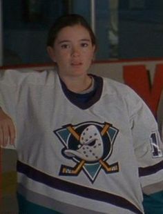 a woman in a hockey jersey standing next to an ice rink with her hands on her hips