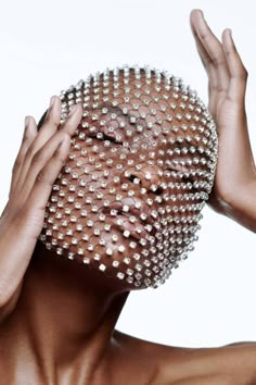 a woman holding her head covered in lots of silver studded balls and covering her face with both hands