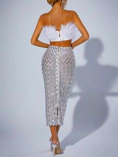 a woman in a white crop top and silver skirt with feathers on the bottom,