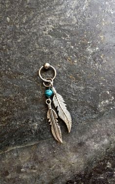 a silver feather charm with turquoise beads on a stone surface in front of a rock