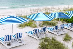 blue and white striped beach chairs with umbrellas on the sand at an empty beach