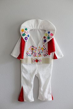 a white and red outfit hanging on the wall next to a pair of pants with colorful buttons