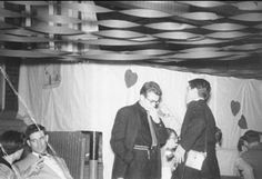 black and white photograph of two men in suit standing next to each other with hearts hanging from the ceiling