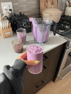 a person holding up a glass with purple liquid in it on a kitchen counter top