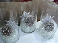 three clear glass vases with pine cones in them