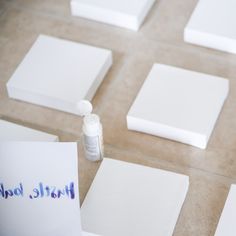 several square pieces of white paper sitting on top of a floor next to a bottle