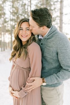 a pregnant couple cuddles in the snow while holding each other's belly