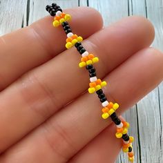 a hand holding a beaded bracelet made out of candy corn and black, orange, yellow and white beads