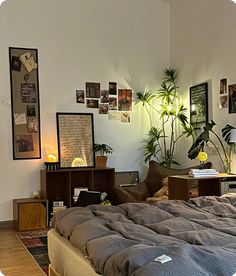 an unmade bed in a room with pictures on the wall and plants behind it