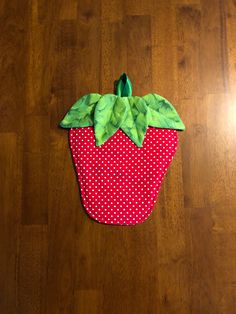 a red and white polka dot covered strawberry sitting on top of a wooden floor