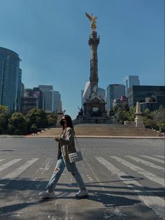 a woman walking across a street in front of a statue