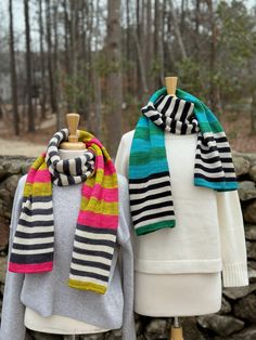 two knit scarves on mannequins in front of trees and stone wall