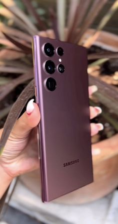 a woman holding up a purple samsung phone in front of a potted plant with green leaves