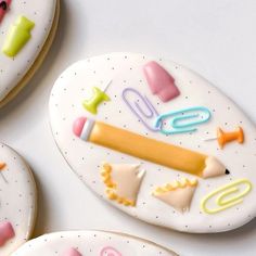 three decorated cookies with different shapes and colors on top of a white surface, one is shaped like a pencil, the other has writing utensils