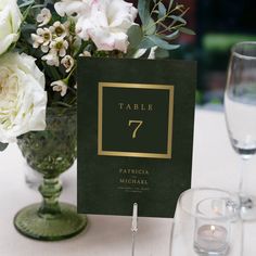 a table number is placed next to a vase with white flowers and wine glasses on the table